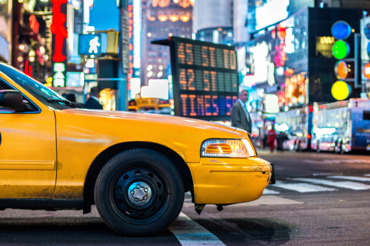 Gelbes Taxi auf den bunten Stra&szlig;en von New York in der Nacht, im Hintergrund funkeln die Lichter der Stadt