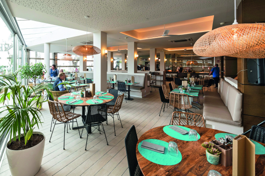 Blick in ein Restaurant mit braunen Tischen und Korbst&uuml;hlen